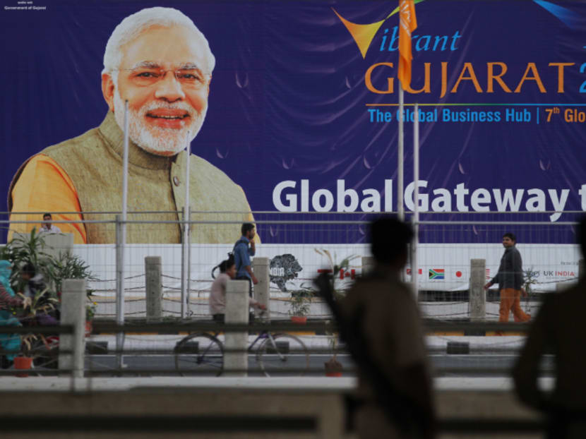 Indian policemen stand guard as people walk past a hoarding with a portrait of Indian Prime Minister Narendra Modi, advertising the Vibrant Gujarat Summit 2015 in Gandhinagar, India, Friday, Jan. 9, 2015. U.S. Secretary of State John Kerry is scheduled to attend the three-day summit that starts Sunday. Photo: AP