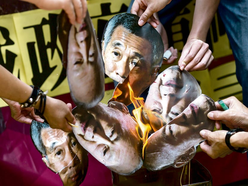 Protesters burn pictures of Singapore's first Prime Minister Lee Kuan Yew and his son and current Prime Minister Lee Hsien Loong to demand the release of Singaporean teenager Amos Yee, outside the Singapore Consulate in Hong Kong, China July 5, 2015. Photo: Reuters