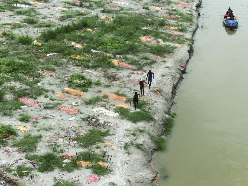 Fishermen pull a boat as they walk amidst shallow graves of people buried on the banks of the Ganges River during the Covid-19 pandemic near a cremation ground in Allahabad, India on June 25, 2021.