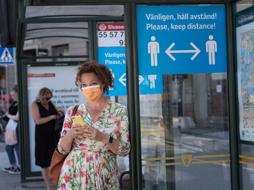 A woman wears a face mask as she waits at a bus stop with an information sign asking people to keep social distance due to the Covid-19 pandemic on June 26, 2020 in Stockholm, Sweden.