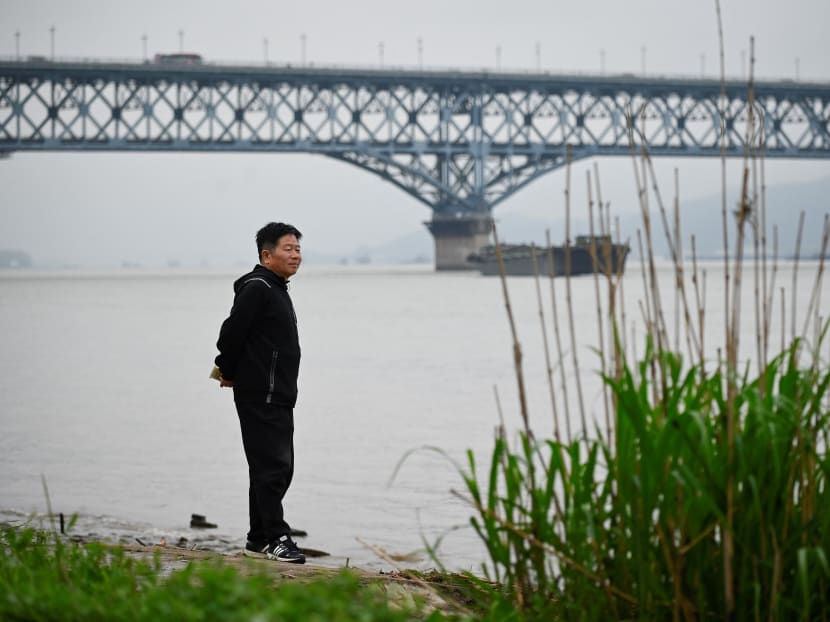 Volunteer Chen Si looks out from the riverside of the Yangtze river, with the Nanjing Bridge in the background, in Nanjing in China's Jiangsu province on April 1, 2021.