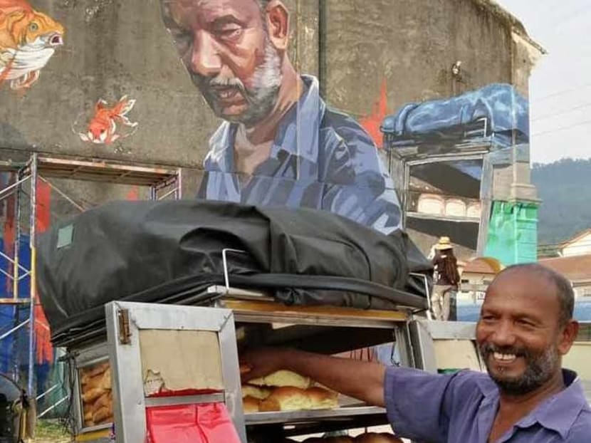 Mr Muniandi stands in front of a mural of him done by street artist Andhar A. Samah.