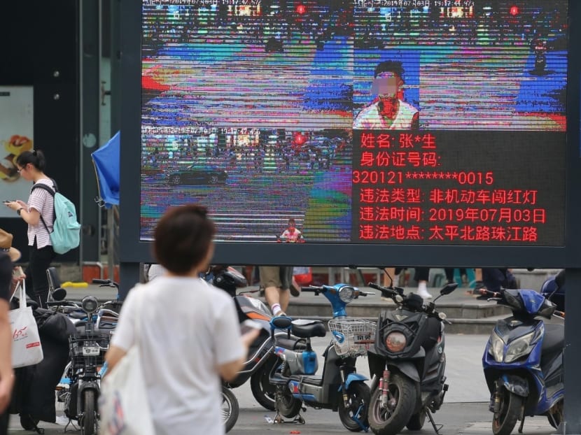 Pedestrians walk across a crossroad as a big electronic screen supported by face-recognition system shows the image of a jaywalker at the intersection in Nanjing city, east China's Jiangsu province on July 4, 2019.