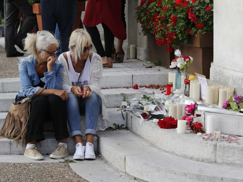 Two women sit near candles and flowers displayed in front of the city hall of the Normandy city of Saint-Etienne du Rouvray. Photo: AFP