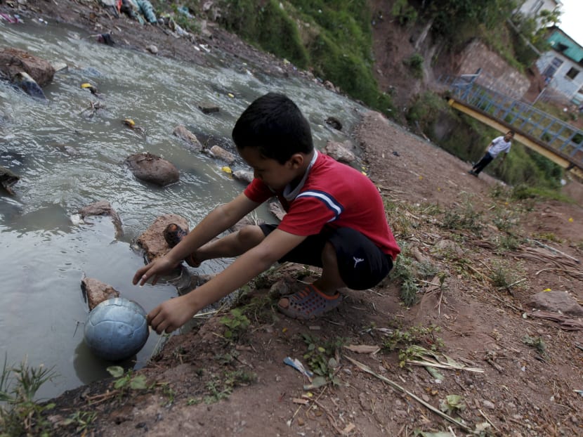 A boy grabs a ball that fell into a creek while playing football with a friend at a slum in Tegucigalpa Jan 27, 2016. Photo: Reuters