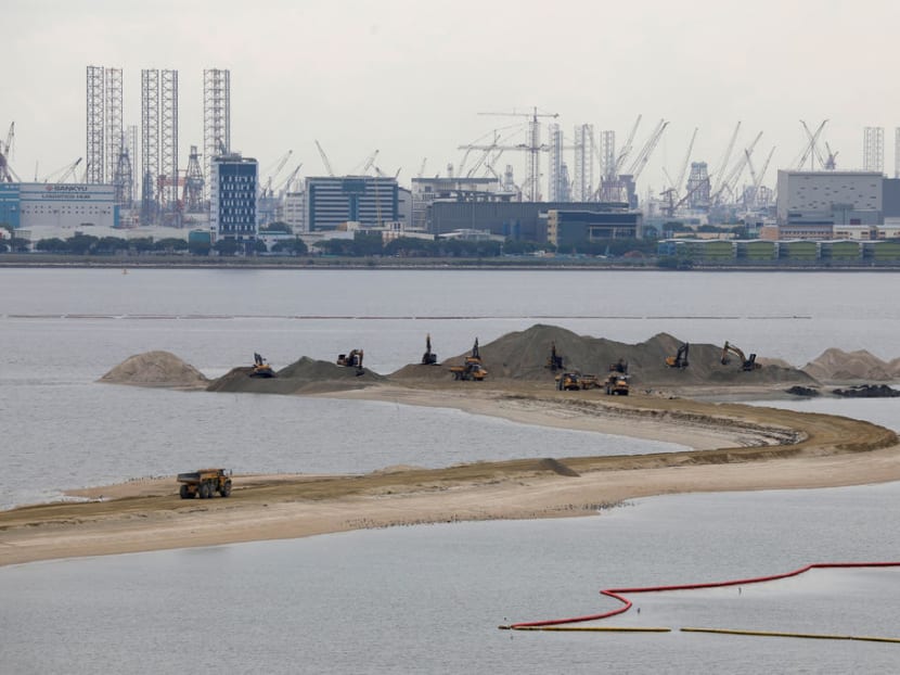 Trucks carry sand at land reclamation area overlooking Singapore's Tuas industrial area.