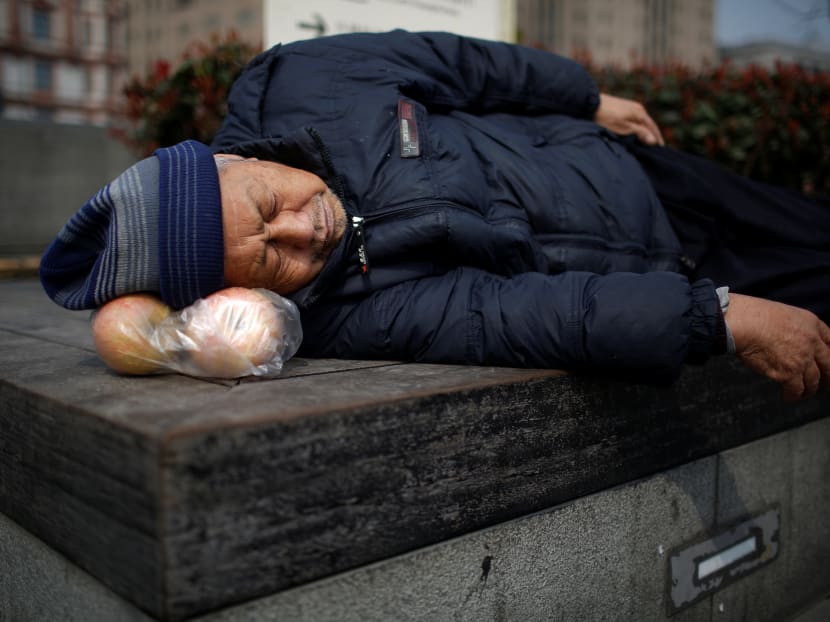A man sleeps at a park, resting his head on a bag of apples, in Shanghai, China. Photo: Reuters