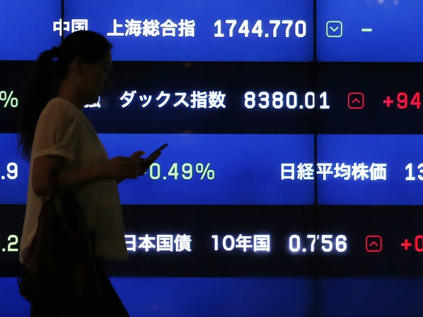 A woman walks past a screen showing market indices in Tokyo August 22, 2013. Photo: Reuters