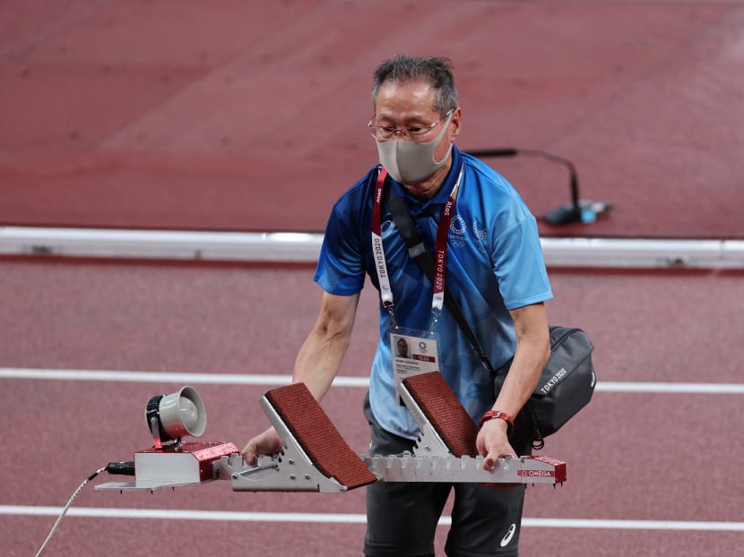 In this file photo taken on July 30, 2021 in Tokyo, an elderly volunteer sets up a track starting block during the athletics event of the Tokyo 2020 Olympic Games at the Olympic Stadium.