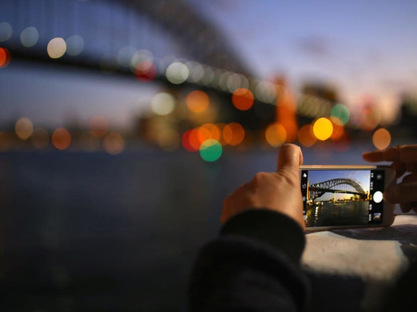 A tourist takes a photograph on their iPhone of the Sydney Harbour Bridge at sunset on a spring day in central Sydney. Photo: Reuters