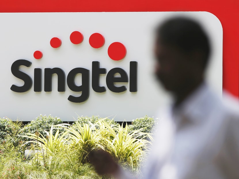 A man using his mobile phone passes a Singtel signage at their head office in Singapore. Photo: Reuters