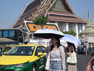 Tourists shield themselves from the sun with umbrellas to combat the heat outside Wat Pho Buddhist temple in Bangkok on April 1, 2024. 