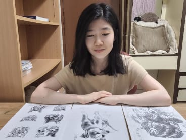 The author is seen here with photocopies of the drawings made by a janitor from her primary school which she has kept. 