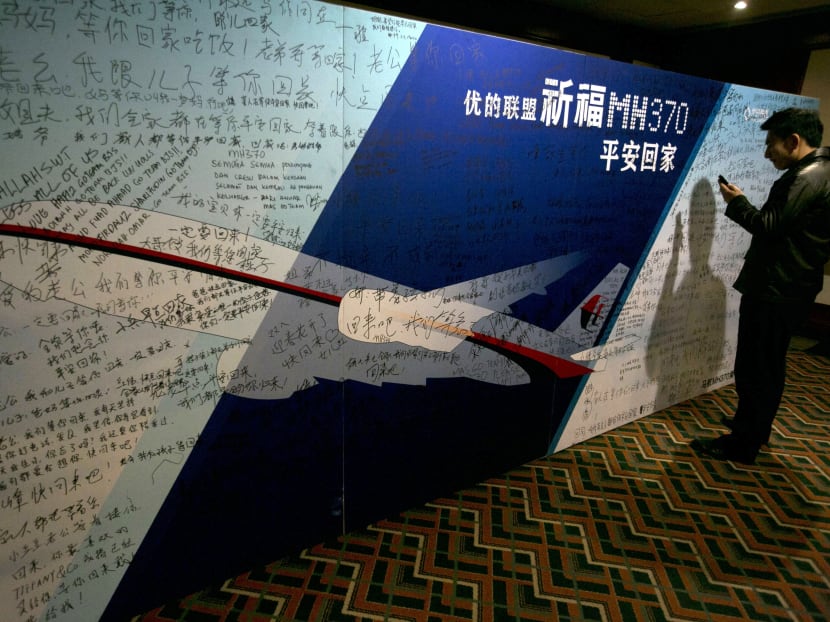 A man uses his mobile phone near a board with the characters "Pray for MH270 safe return" meant for relatives and workers to write their prayers and well wishes in a room reserved for relative of Chinese passengers aboard the missing Malaysia Airlines, MH370 in Beijing, China, March 24, 2014. Photo: AP