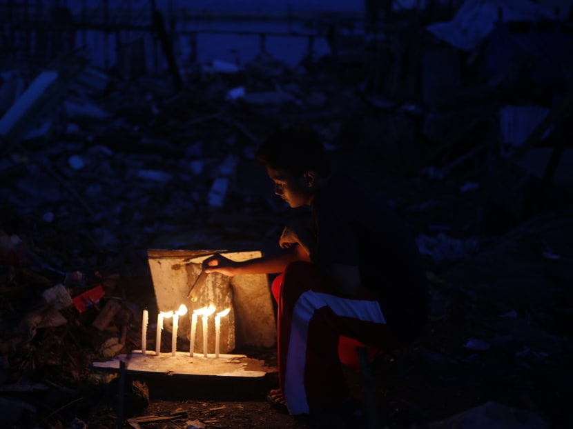 A typhoon survivor lights candles amidst the ruins of destroyed houses to mark 40 days since the death of his relatives in Tacloban city in central Philippines on Dec 17, 2013. Photo: Reuters