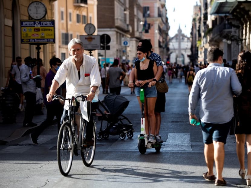 People walk and cycle along a street on the eve of Italy moving into the 'white zone' when it will not be obligatory to wear the mask outdoors in Rome on June 27, 2021.