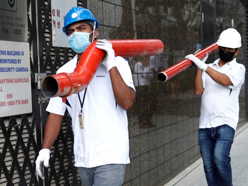 Construction workers wearing masks in precaution of the coronavirus outbreak carry pipes as they pass a building in the Central Business District in Singapore on Feb 18, 2020. Construction workers wearing masks in precaution of the coronavirus outbreak carry pipes as they pass a building in the Central Business District in Singapore on Feb 18, 2020.