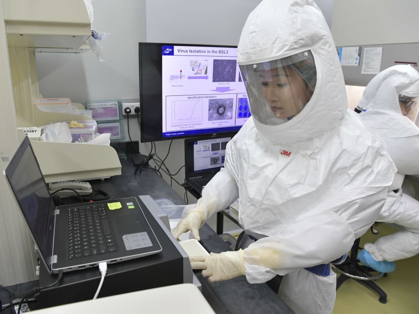 A scientist wearing personal protective equipment with powered air purifying respirator places samples into the polymerase chain reaction machine in the existing DSO biosafety lab.