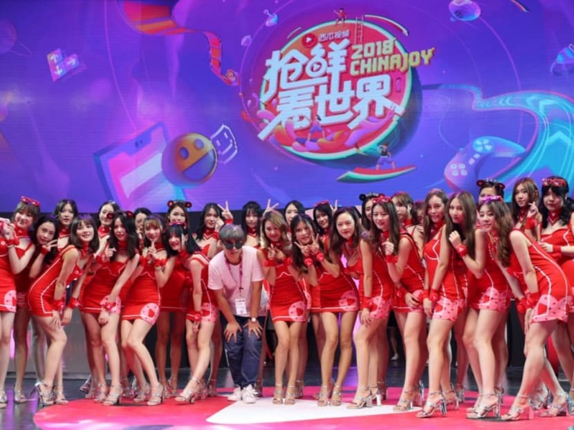 A male staffer poses with showgirls at the booth of live-streaming app Xigua on the last day of ChinaJoy.
