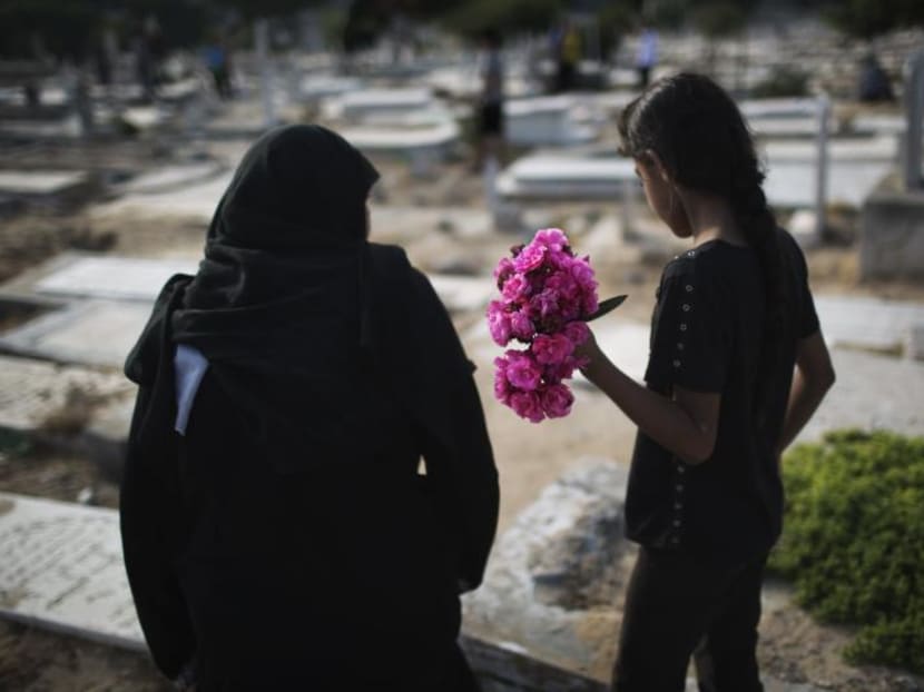 A Palestinian woman and a girl carry flowers to a family grave on Eid al-Fitr at a cemetery in Gaza City July 28, 2014. Photo: Reuters