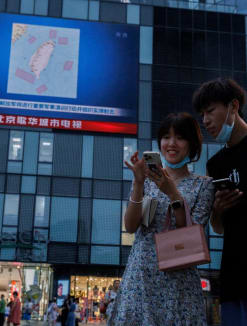 People stand in front of a screen showing a CCTV news broadcast, featuring a map of locations around Taiwan where Chinese People's Liberation Army (PLA) will conduct military exercises and training activities including live-fire drills, at a shopping center in Beijing on Aug 3, 2022. 