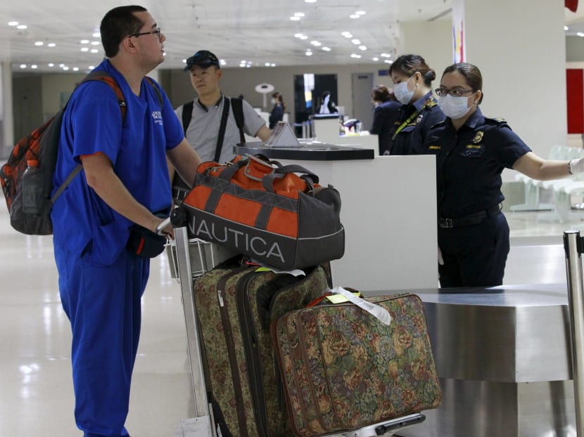 A custom inspector wearing a face mask gestures to a flight passenger arriving from South Korea, as she shows the way out upon arrival at Ninoy Aquino International Airport in Manila, June 9, 2015. Photo: Reuters