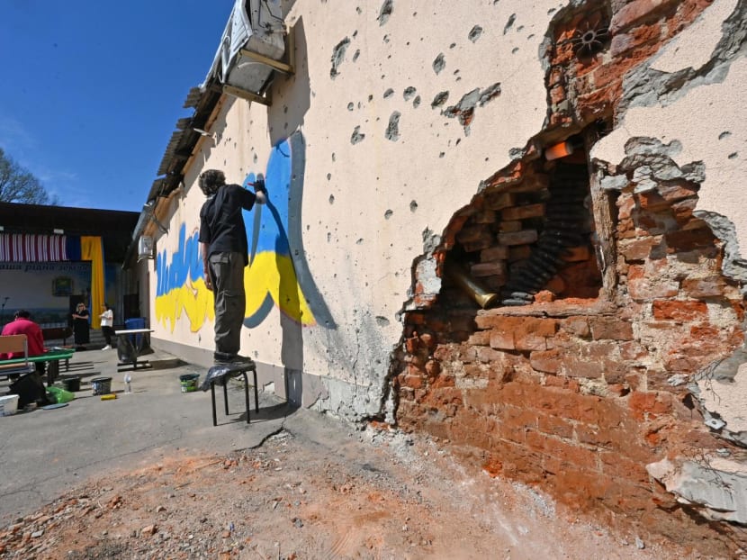 An artist paints the village name in the colors of the Ukrainian national flag on a wall of a local house, partially damaged during the shelling in the village of Tsirkuny, Kharkiv region, Ukraine
