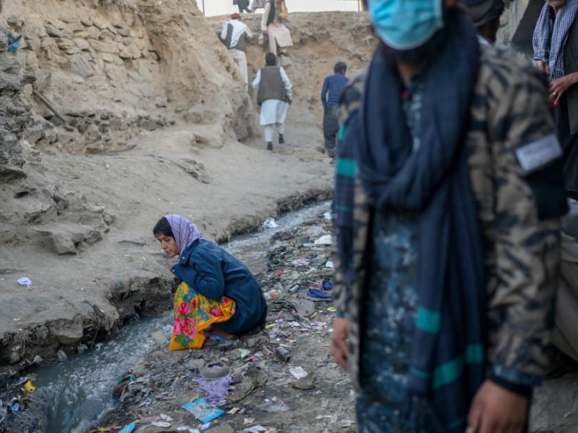This picture taken on Oct 9, 2021 shows a drug addict woman sitting next to a canal near a bridge where hundreds of addicted people gather in Kabul.