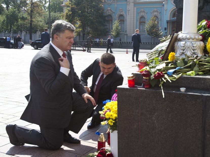 Ukraine's President Petro Poroshenko, left, and parliament speaker Volodymyr Groisman lay flowers by the photo of a police officer who was killed in a Monday clash, in front of Parliament in Kiev, Ukraine, Sept 1, 2015. Photo: Pool photo via AP