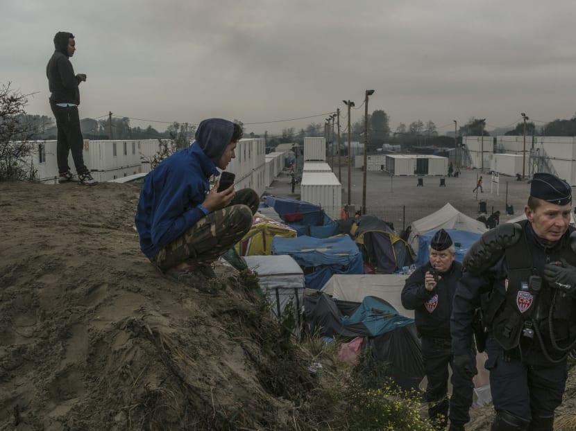 Refugees who mounted a small hill for a better cellphone signal, eye police in a makeshift camp where 6,000 or more have been living in Calais, France, Oct 26, 2016. Photo: The New York Times