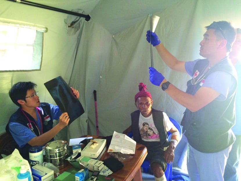 Mr Funchu Tamang (centre), 101, with Dr Raymond Lim (left) and Mr Jeffrey Tan, a paramedic on the Singapore Red Cross team, was one of several Nepalese who streamed into the medical camp set up by the Singapore Red Cross with Qatar Red Crescent. Photo: Siau Ming En