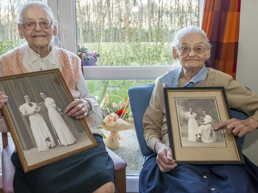 Centenary twins, Paulette Olivier (L) and Simone Thiot (R) pose with an old picture of their 20 years inside their room at the retirement home "Les Bois Blancs" on February 11, 2016.  Photo: AFP