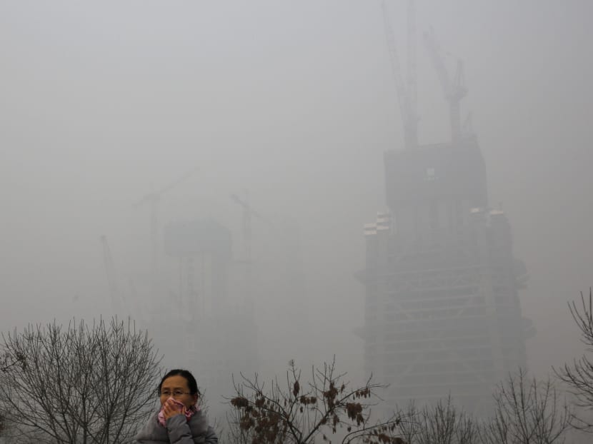 A woman using a cloth to cover herself from pollutants walks past a construction building on a heavily polluted day in Beijing, Monday, Nov. 30, 2015. Photo: AP