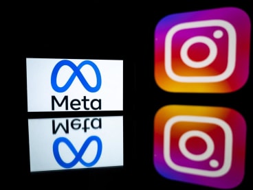 This picture taken on January 12, 2023 shows a smartphone and a computer screen displaying the logos of Instagram app and its parent company Meta.
