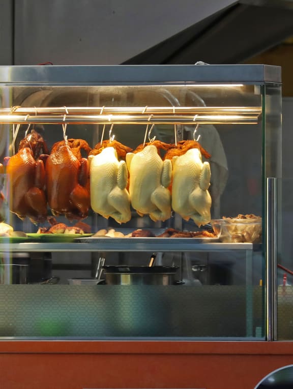 A man walking past a chicken rice stall in Chinatown.