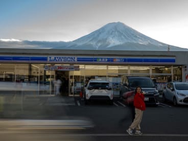 A tourist posing in front of a convenience store with Mount Fuji in the background, in the town of Fujikawaguchiko, Yamanashi prefecture on Jan 1, 2024. 