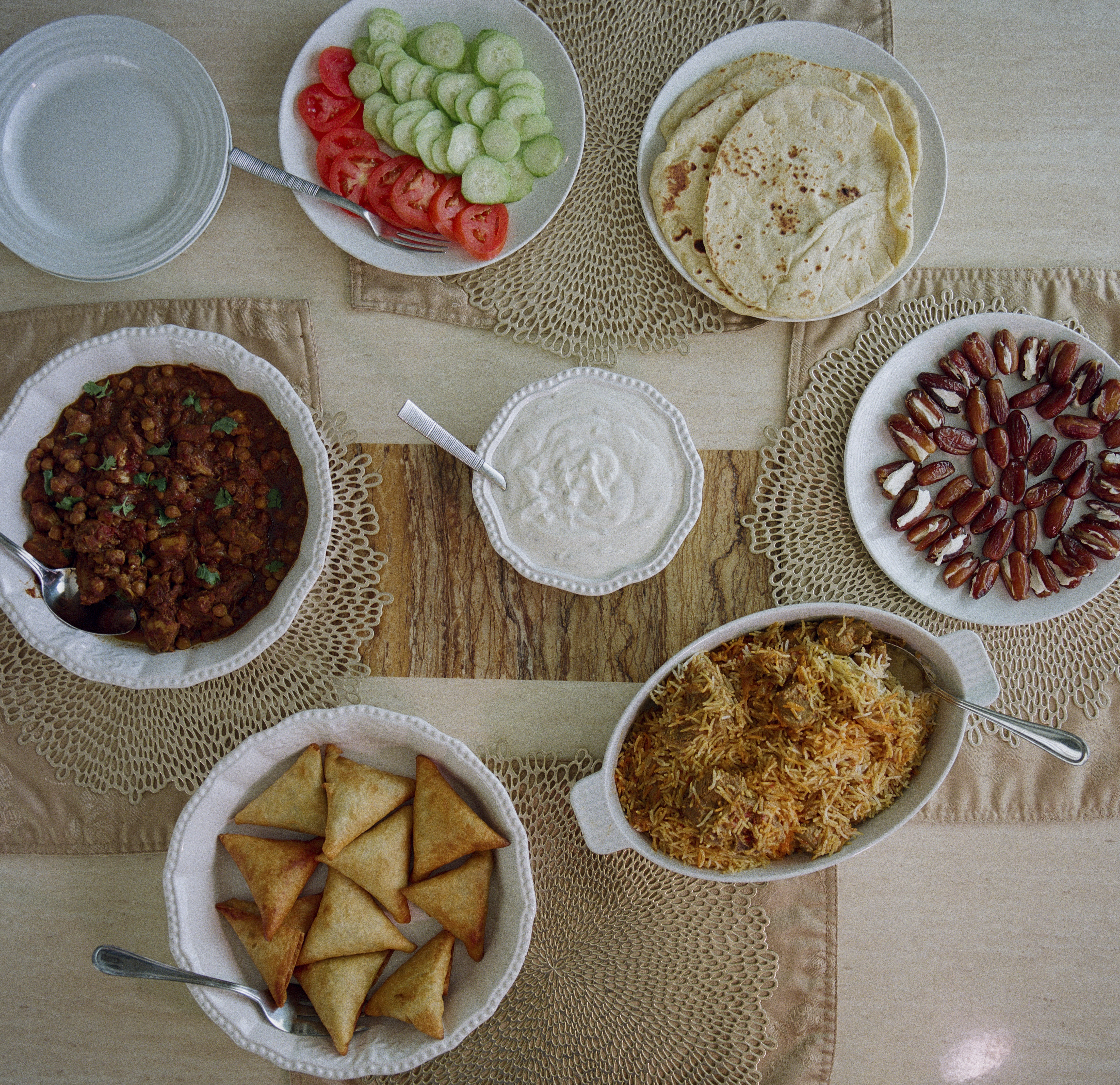 When the Joneses break the fast during Ramadan, their favorites include (clockwise from left) chickpea curry, fresh vegetables, naan, stuffed dates, biryani beef samosas and (center) raita.